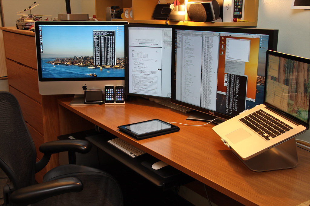 Multiple monitors and a laptop on a wooden desk, each screen showing live terminal windows, logs, and document output during active system testing